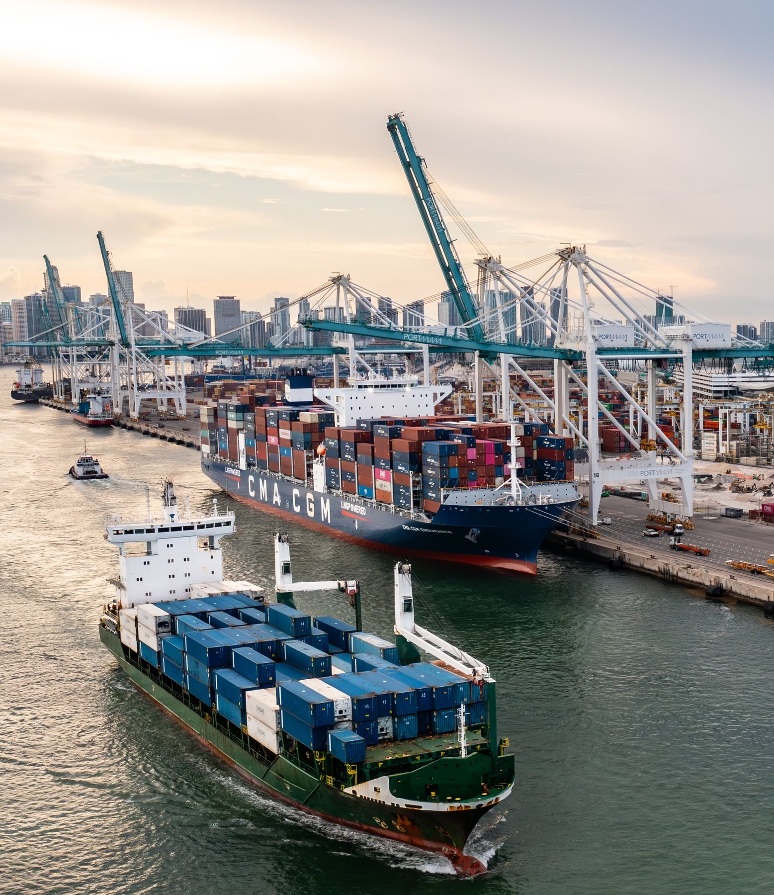 A shallow-draft cargo vessel passing a larger container ship in the PortMiami channel